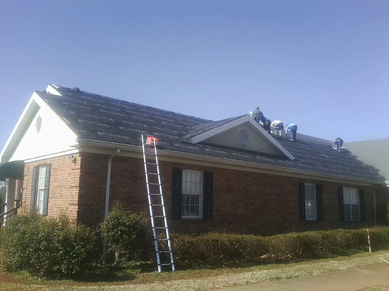 Crew tearing shingles off a brick ranch roof with a ladder set — Metal Roof Repair work by our crew in Dawsonville