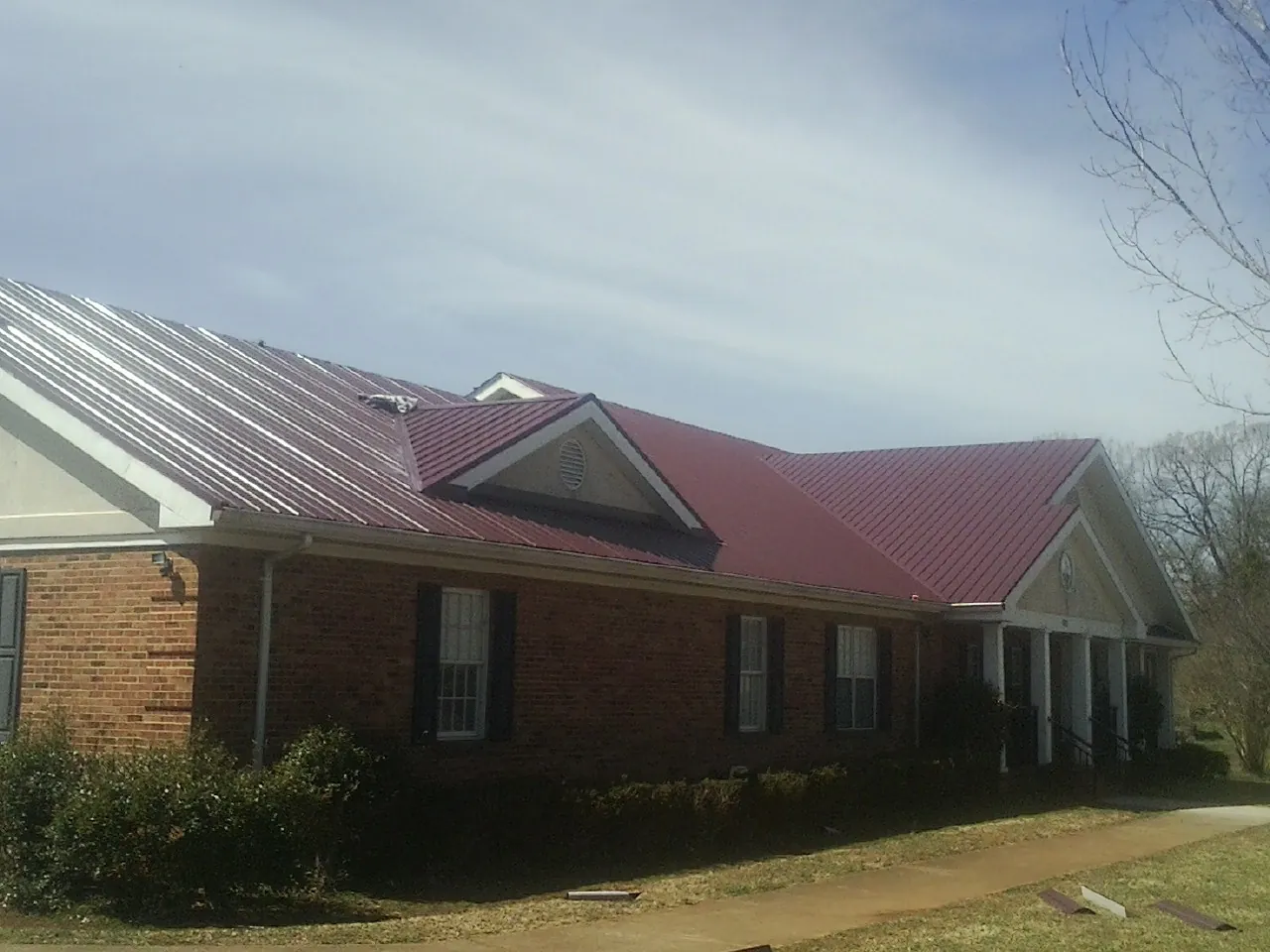 Red metal roof with gabled entries on a long brick building, from a Hail Damage Roof Repair job in Dawsonville