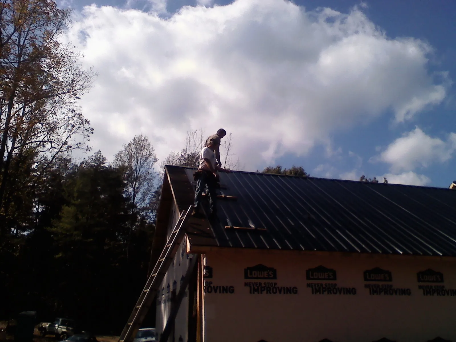 Roofer fastening dark metal panels high against a cloudy sky, from a Roof Inspection job in Dawsonville