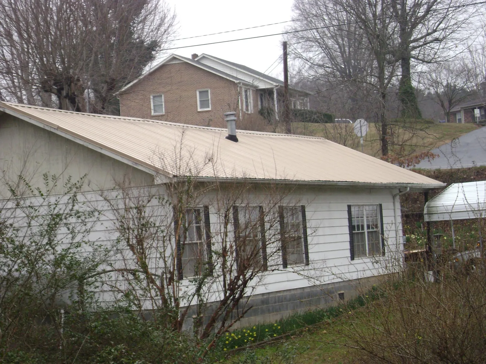 Tan metal roof on a white sided house set into a hillside — Commercial Roofing by Roofing Brothers in Dawsonville